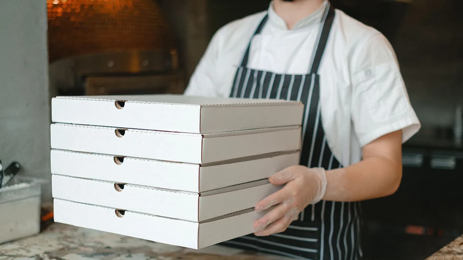 Pizzaiolo con una pila di cartoni d'asporto davanti al forno durante il servizio